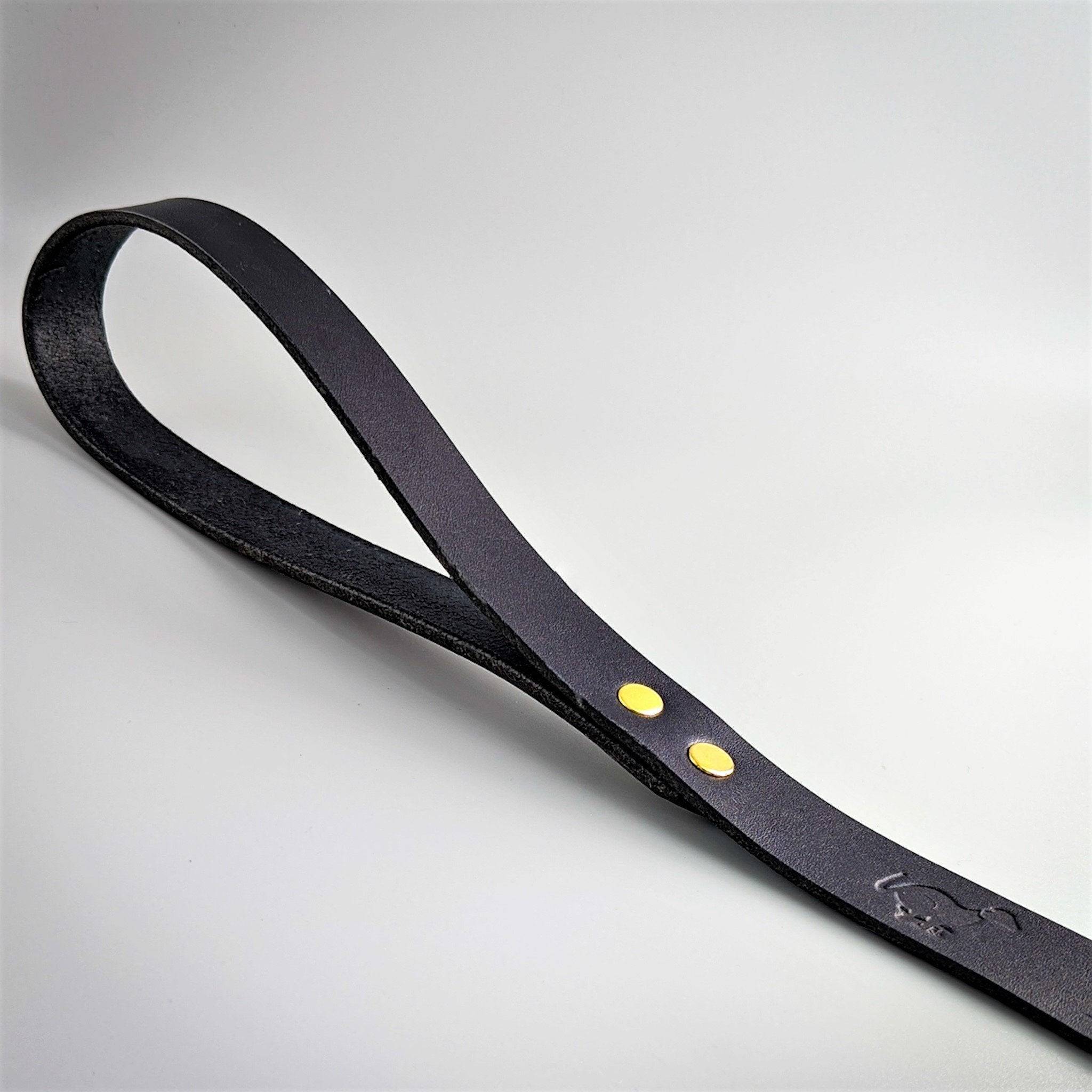 Black leather Cerberus dog lead with brass rivets and embossed logo displayed at angle on clean white background
