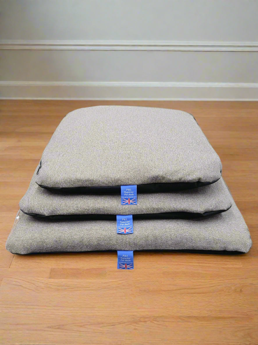 Three grey Orkney tweed dog bed covers stacked on wooden floor showing different sizes with UK quality tags