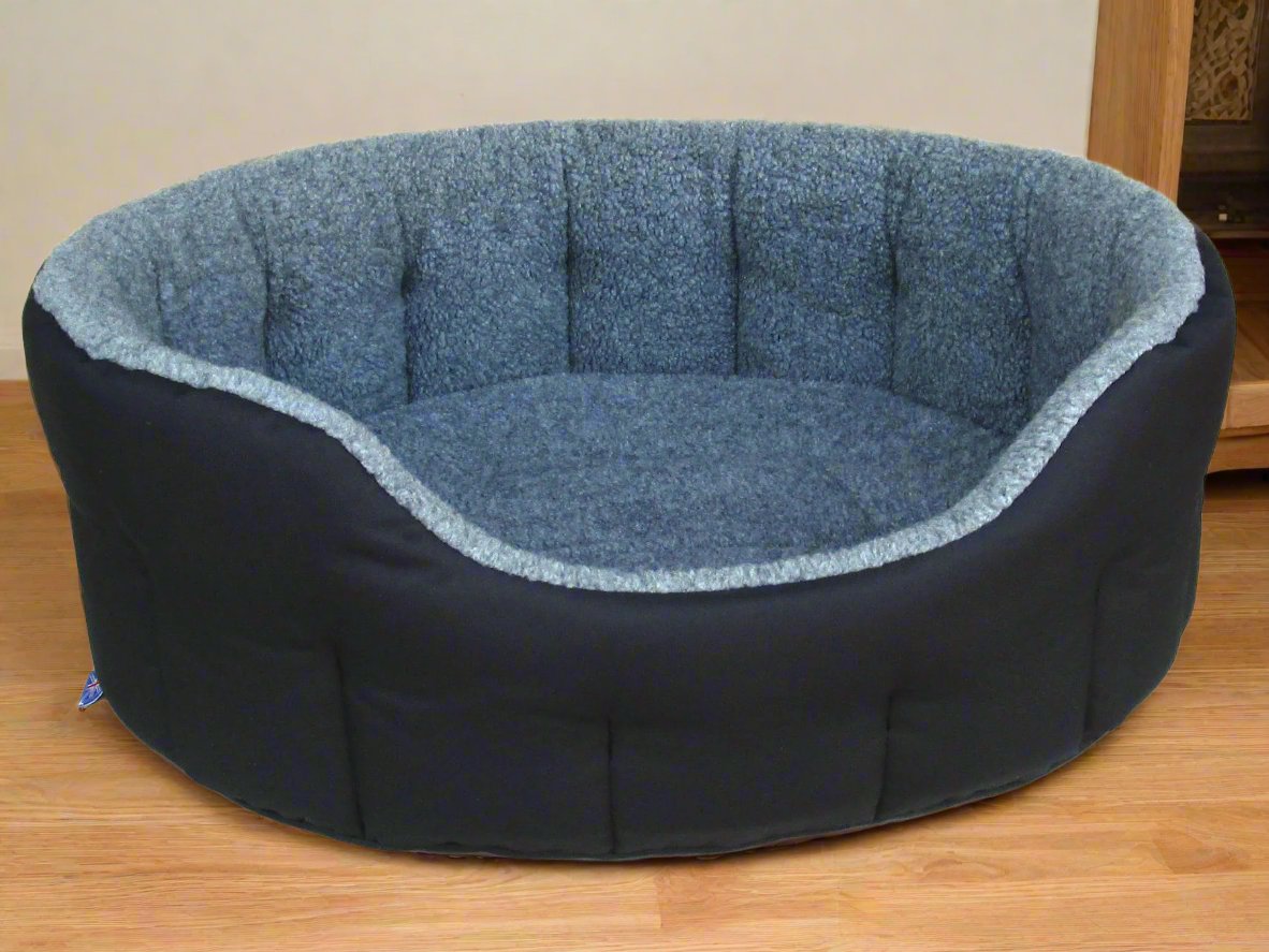 Navy blue oval dog bed with quilted grey fleece lining and bolster sides, handcrafted waterproof design on wooden floor