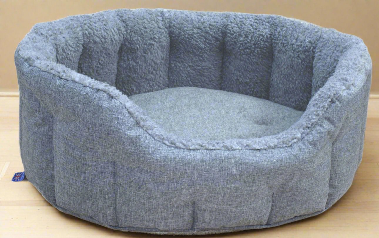 Grey fleece lined oval dog bed with bolster sides and durable fabric exterior on wooden floor