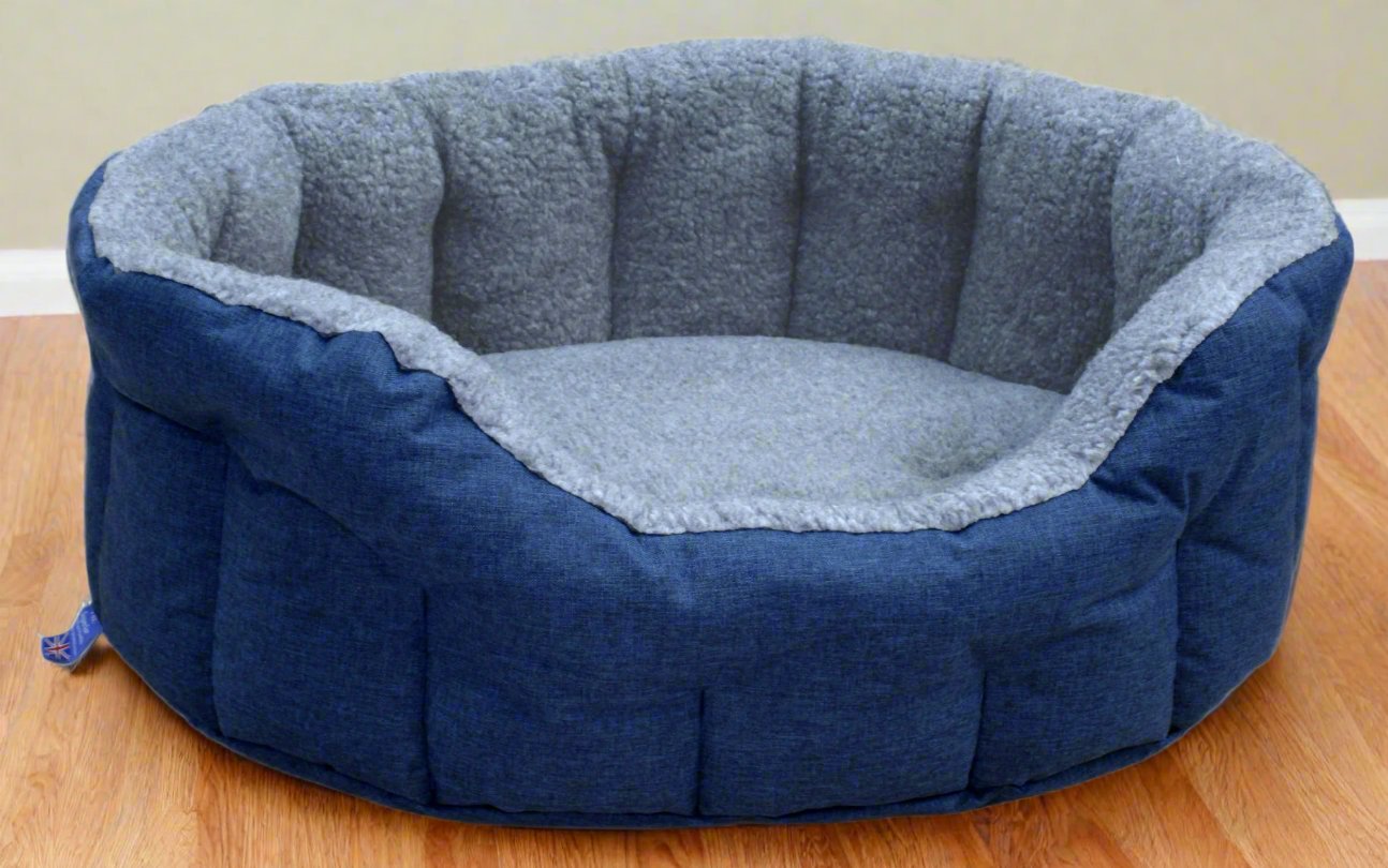 Navy blue oval dog bed with grey fleece lining and quilted bolster sides on wooden floor - waterproof washable design