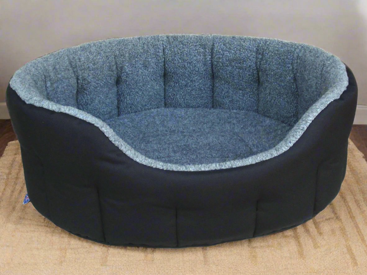 Oval bolster dog bed with black exterior and blue fleece lining, showing quilted comfort design on wooden floor