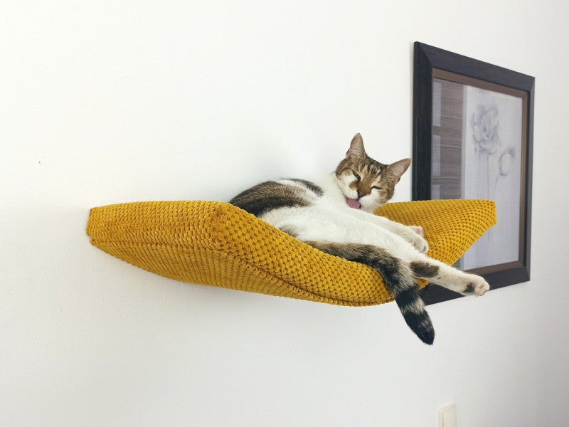 Lifestyle shot of a cat lounging on a mustard yellow Arcing Haven Cat Shelf