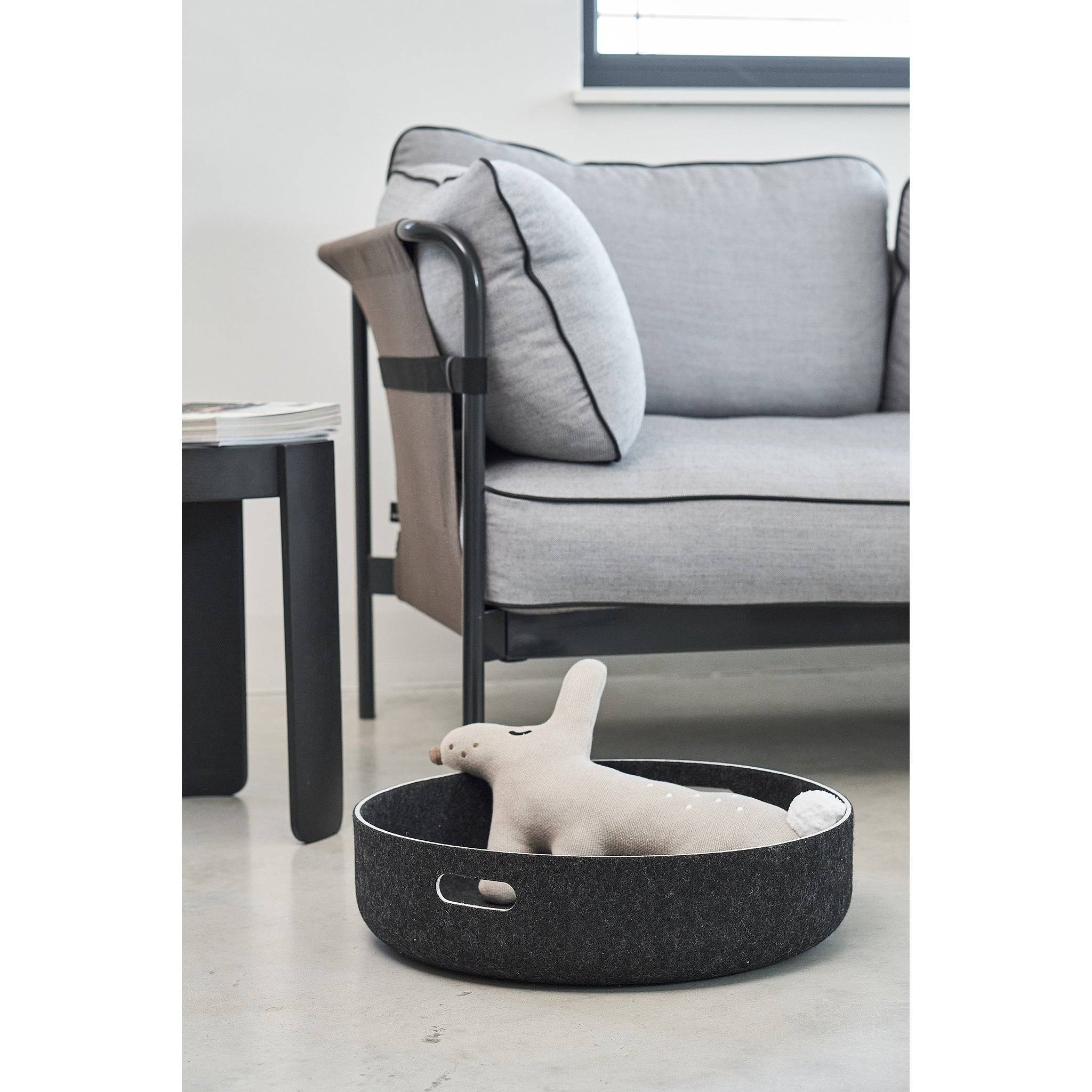 Minimalist dark felt pet toy basket with white plush toy, featuring German design beside contemporary grey sofa