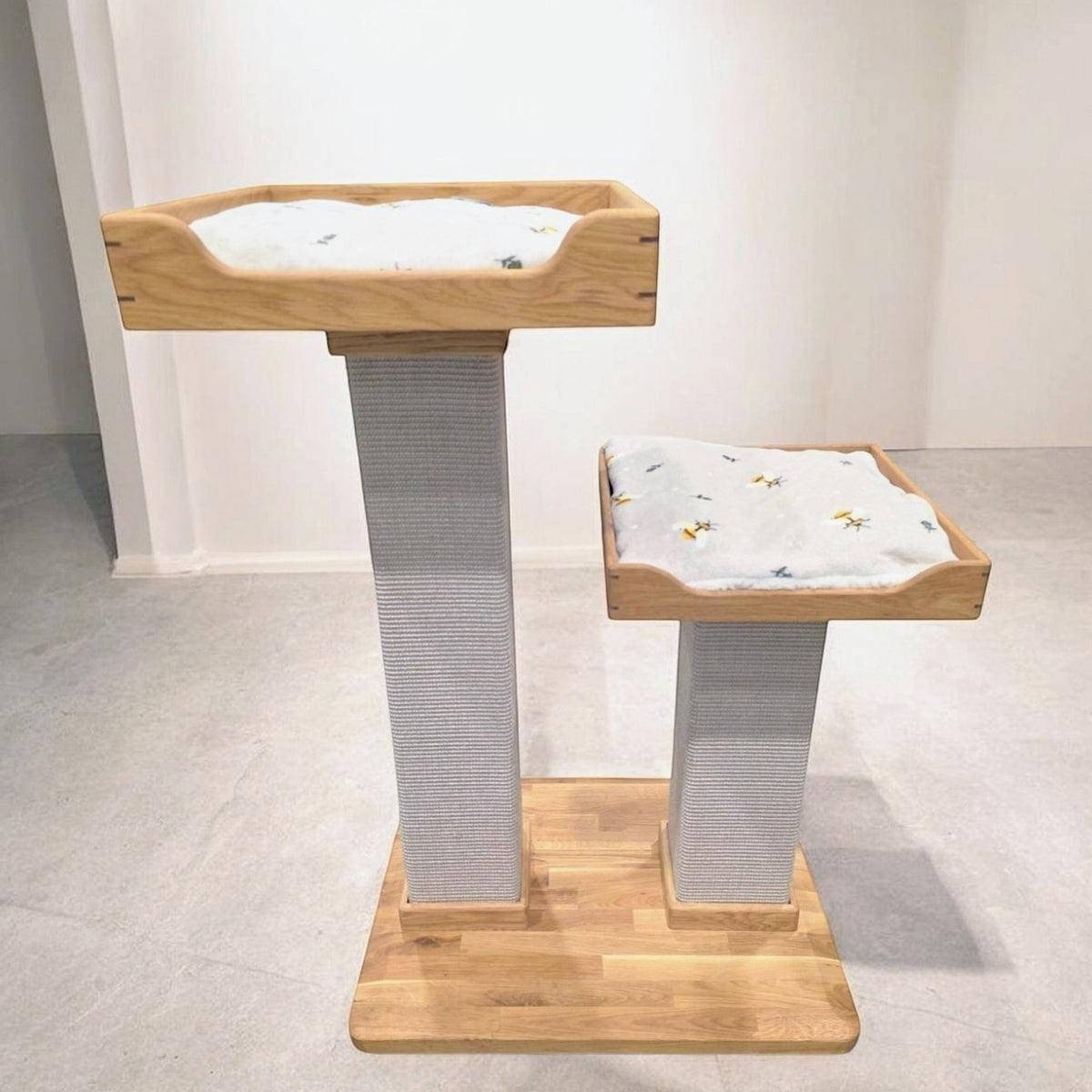 Handmade two-post cat tree with two beds with patterned cushions and a solid oak base, three-quarter view