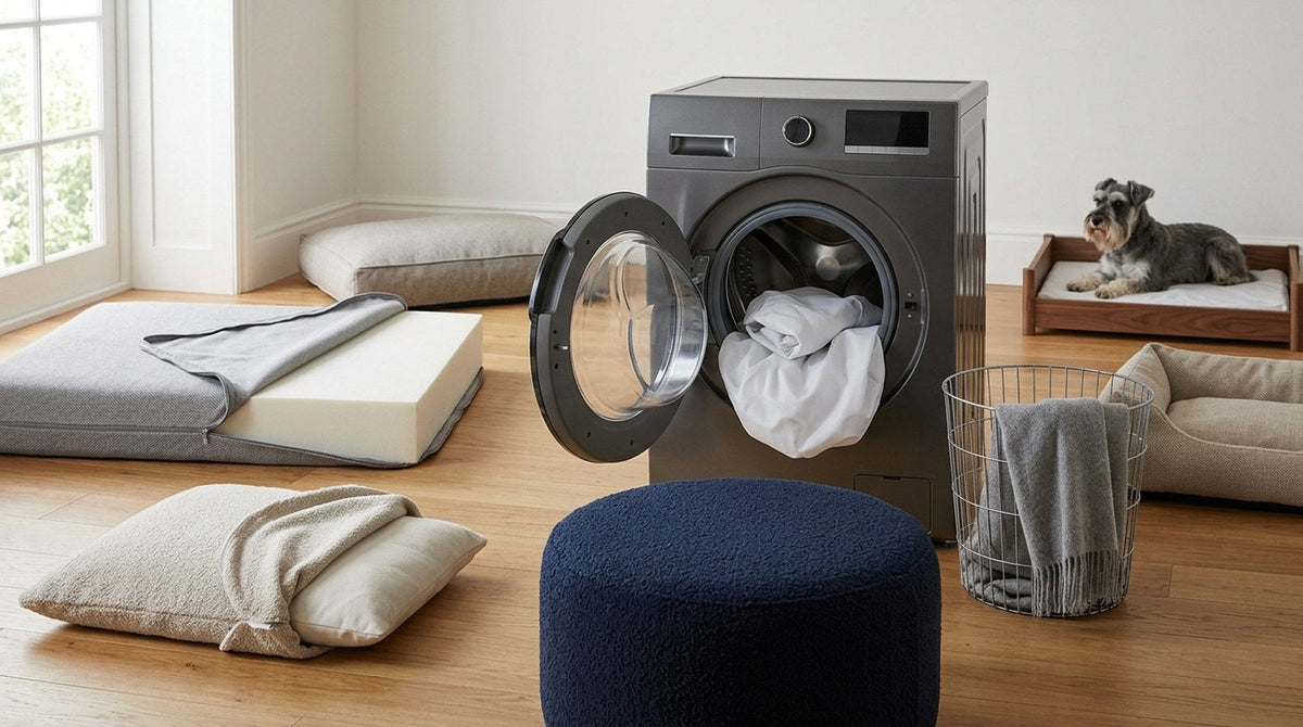 Dog bed covers and a foam mattress laid out beside an open washing machine, with a schnauzer watching from its bed