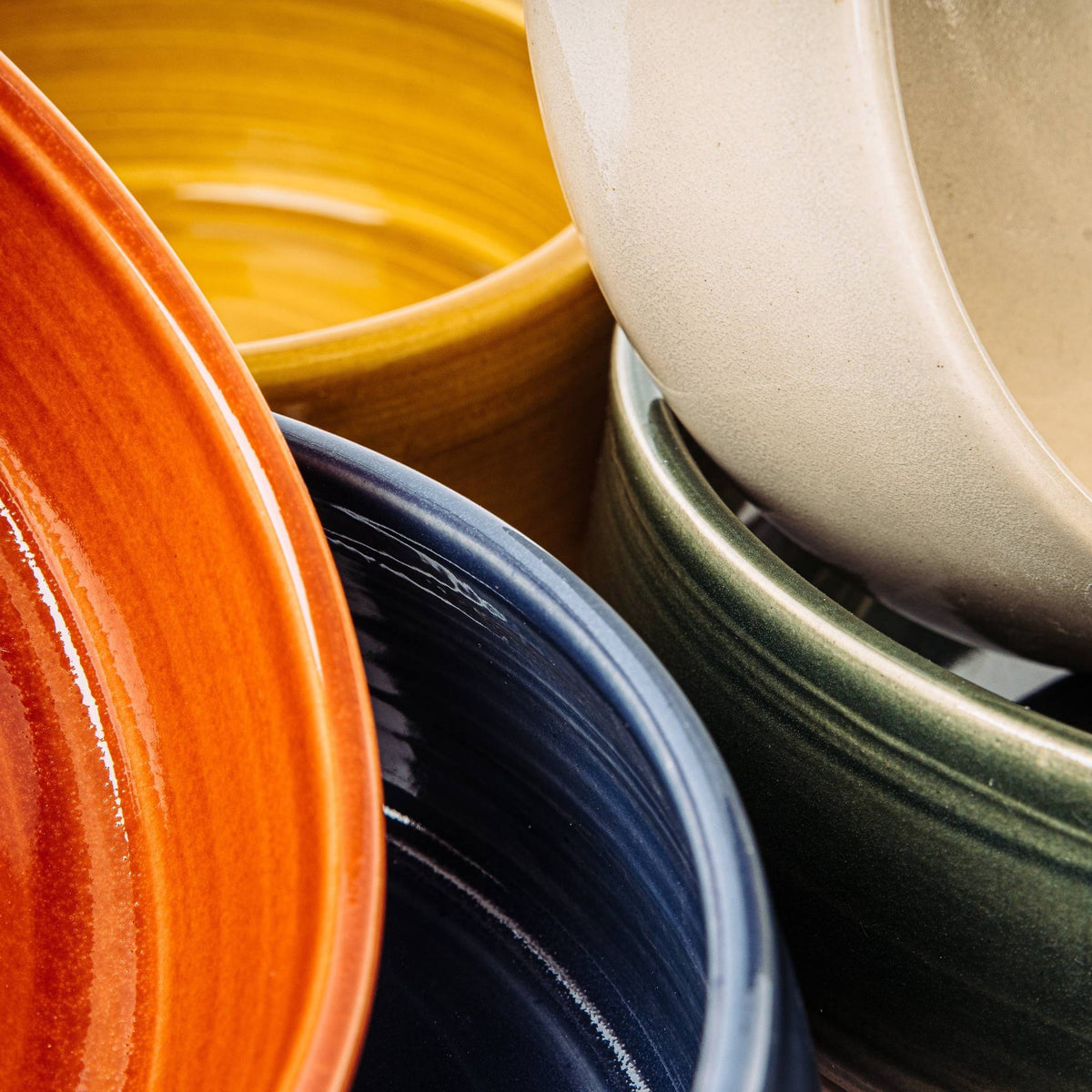 Handmade British stoneware dog bowls by Wirksworth Pottery in vibrant orange, yellow and other glazes, showing the range of colours
