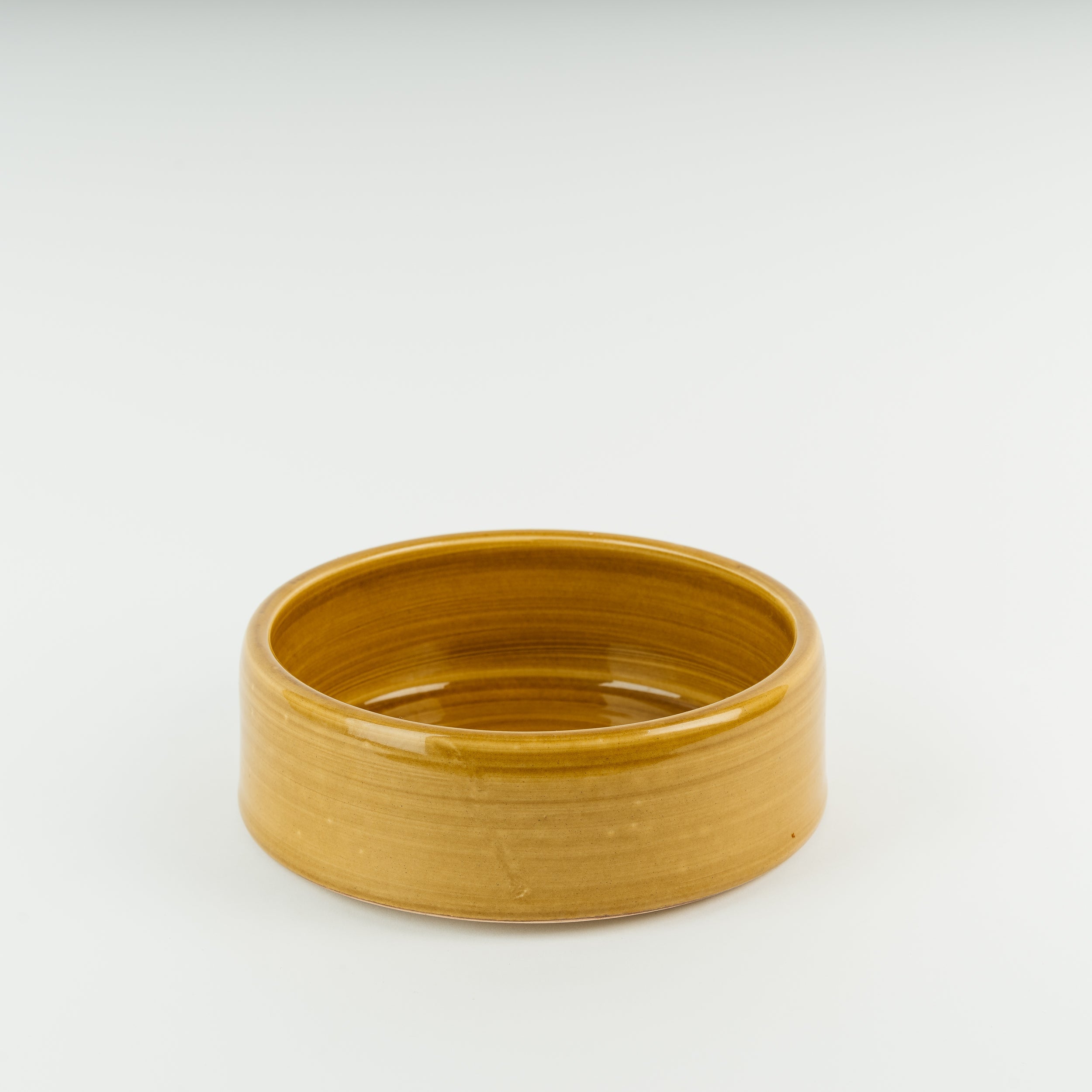 Small handmade stoneware dog bowl in golden glaze showing traditional British pottery craftsmanship and artisan quality