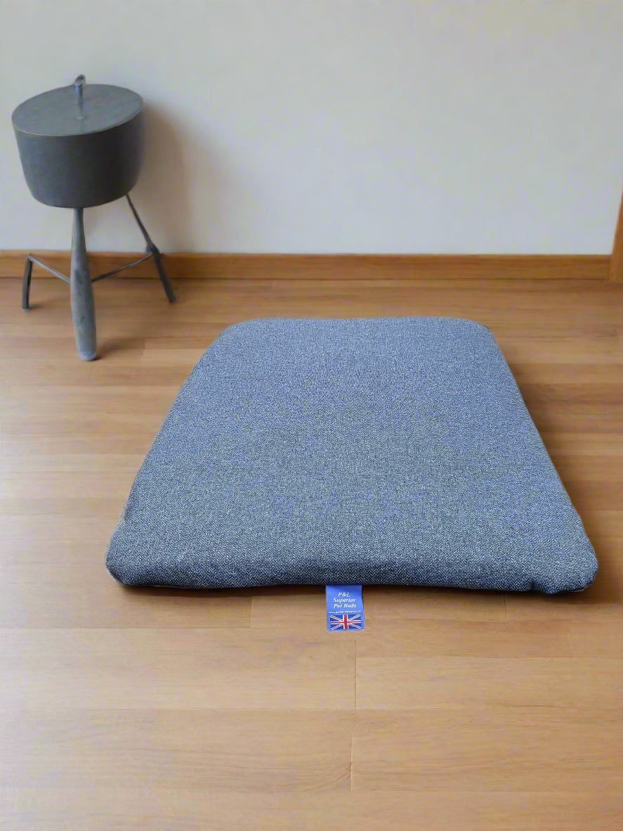 Grey tweed dog bed with removable cover on wooden floor, featuring Union Jack label - premium pet bedding