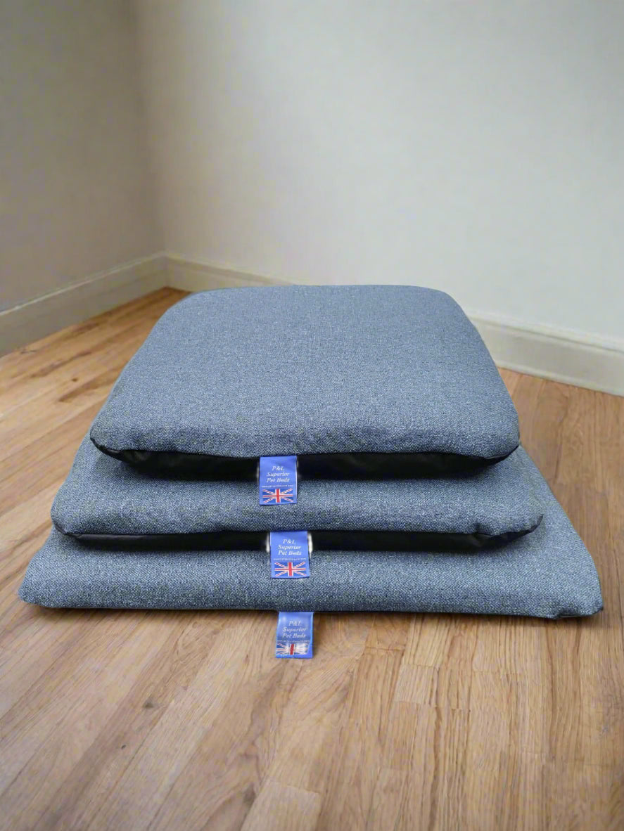 Three grey Orkney tweed dog beds stacked showing removable covers with British flag labels on wooden floor