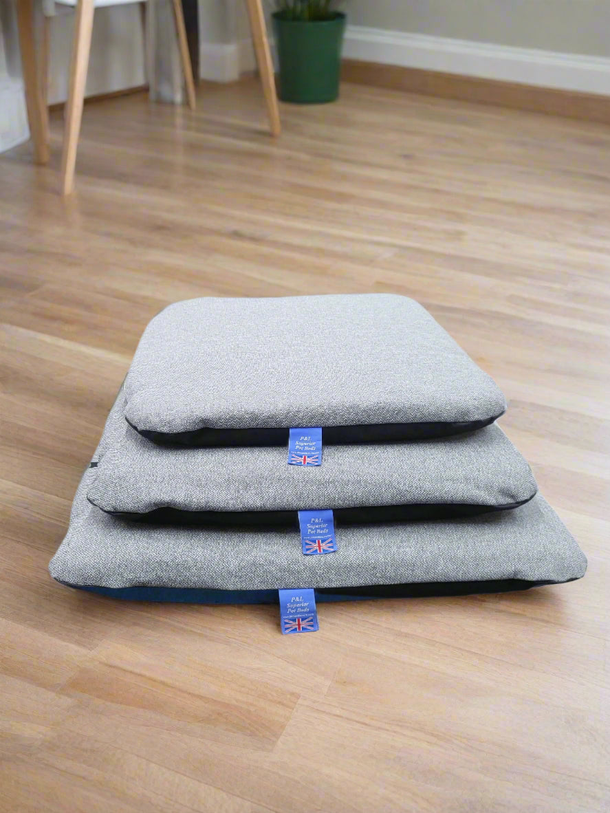 Three grey Orkney tweed waterproof dog beds stacked showing different sizes with Union Jack labels on wooden floor