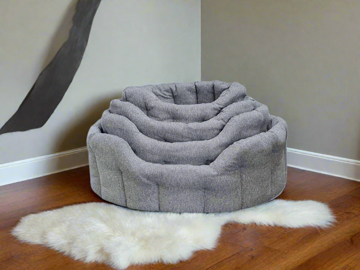 Grey Orkney tweed oval dog beds in graduated sizes stacked together on wooden floor with white sheepskin rug