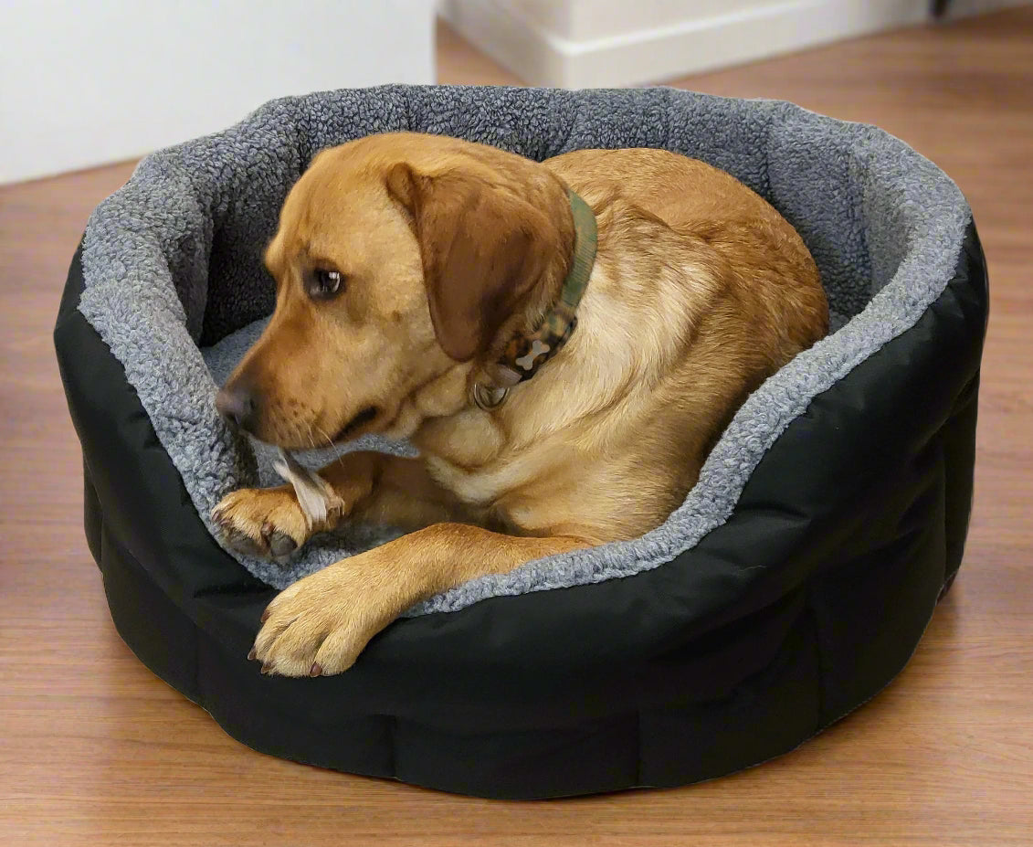 Golden Labrador resting in black waterproof oval dog bed with grey fleece lining and raised bolster sides on wooden floor
