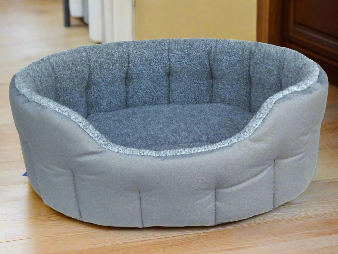 Grey fleece lined oval dog bed with quilted interior and durable outer fabric on wooden floor