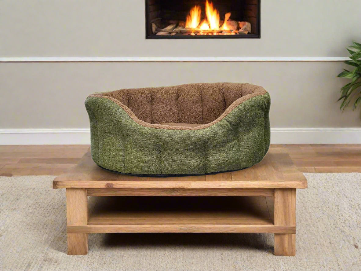 Green tweed dog bed with fleece lining on wooden stand near fireplace - Premium Orkney Tweed Bolster Bed