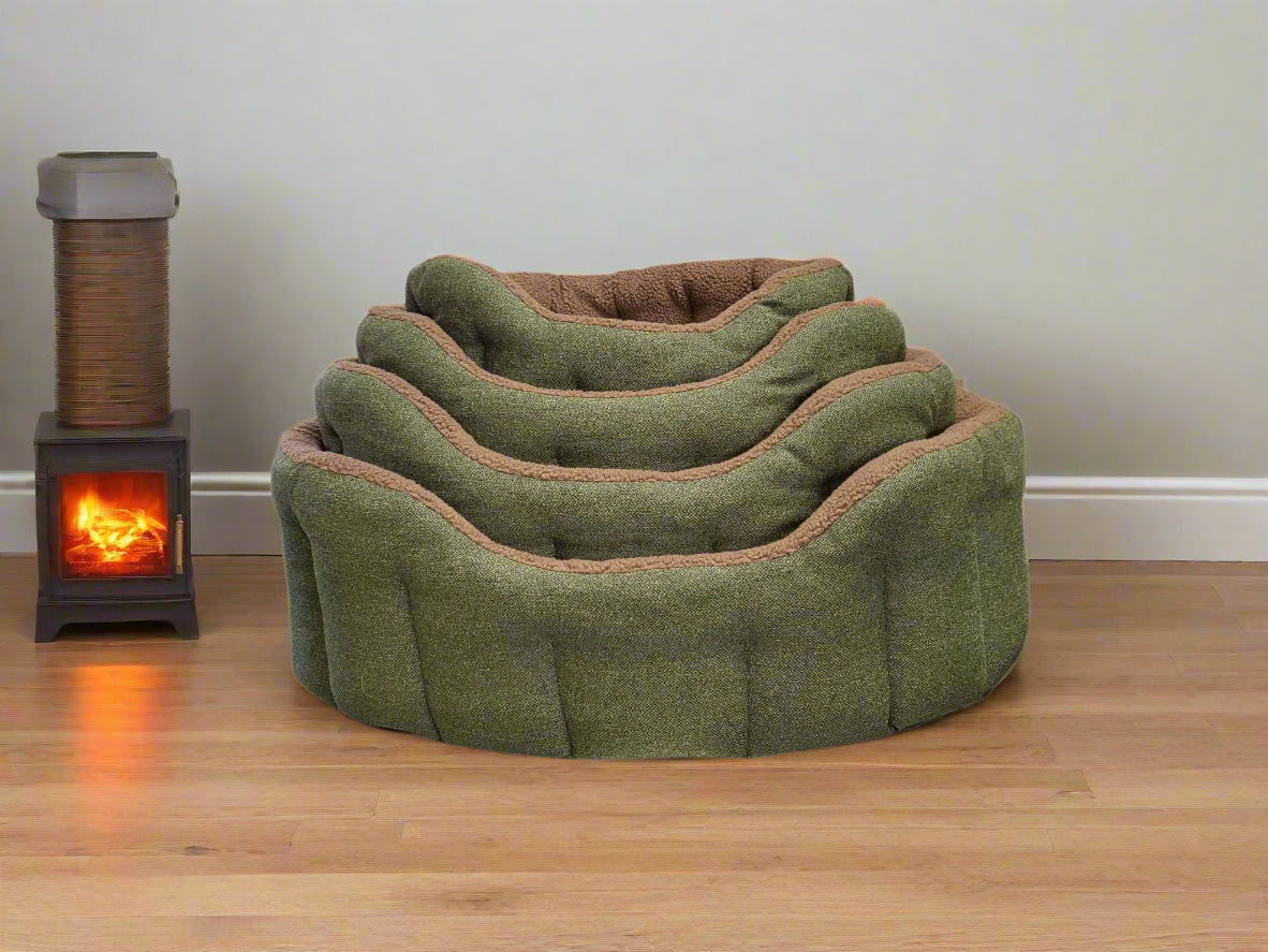Premium green Orkney tweed fleece lined dog bolster bed with tan trim displayed beside wood burning stove on wooden floor