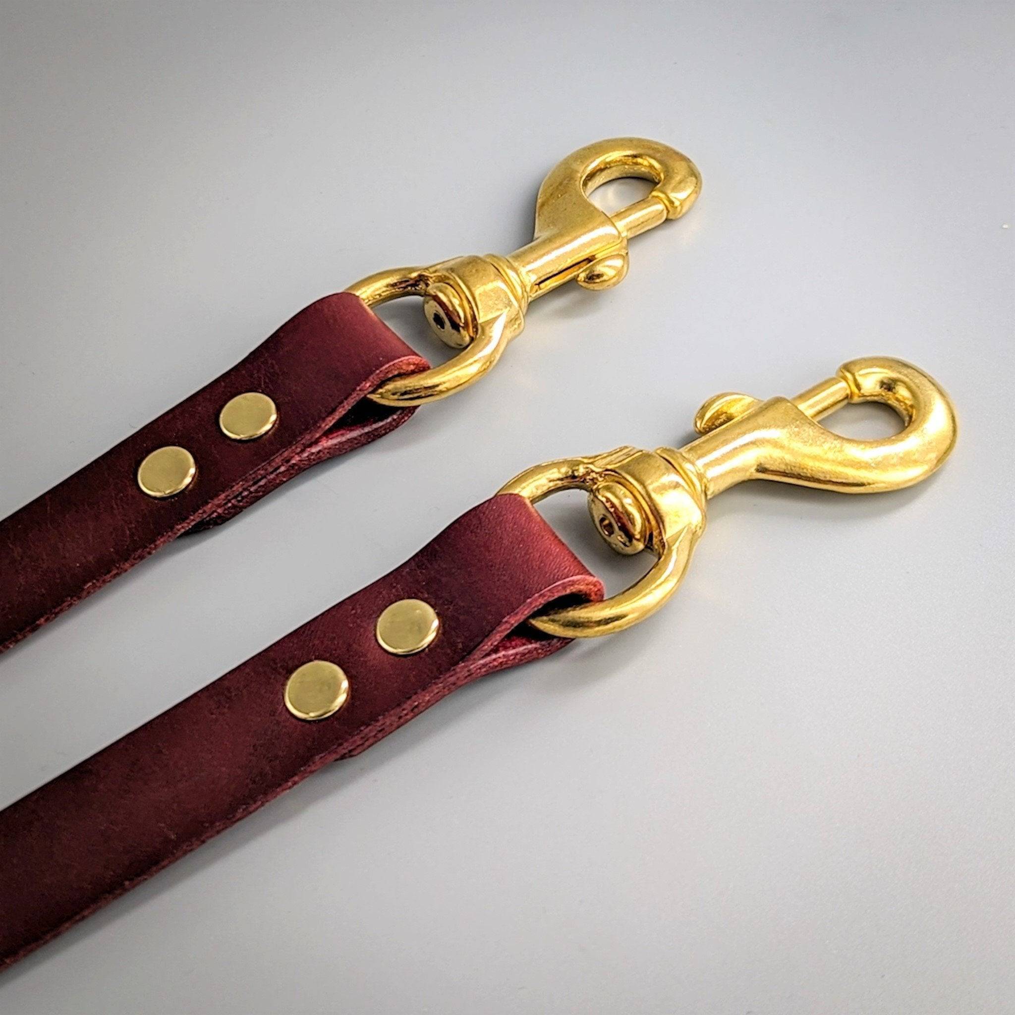 Two burgundy leather training leads with gold swivel clasps and decorative rivets on white background