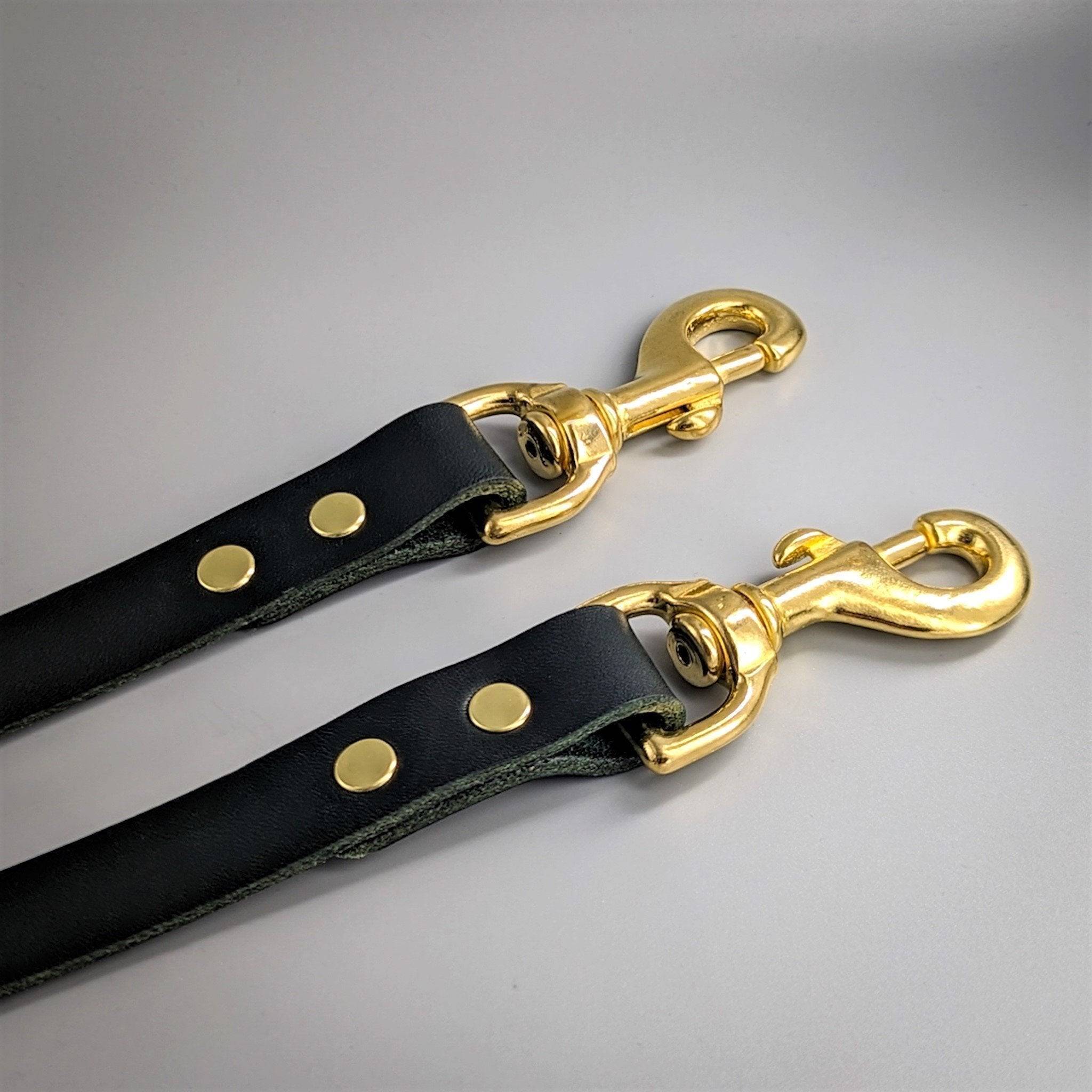 Two black leather training leads with gold brass hardware and swivel clips arranged diagonally on gray