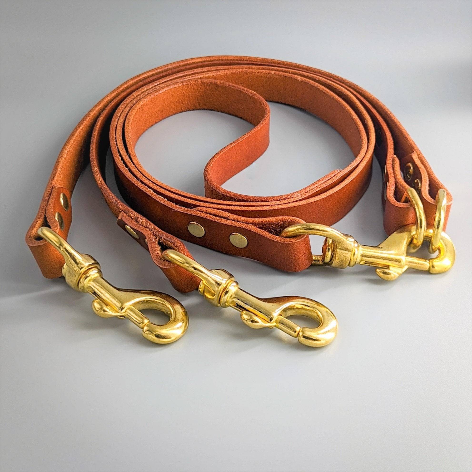 Tan cognac leather Cerberus two dog lead with brass snap hooks and central coupling system on gray background
