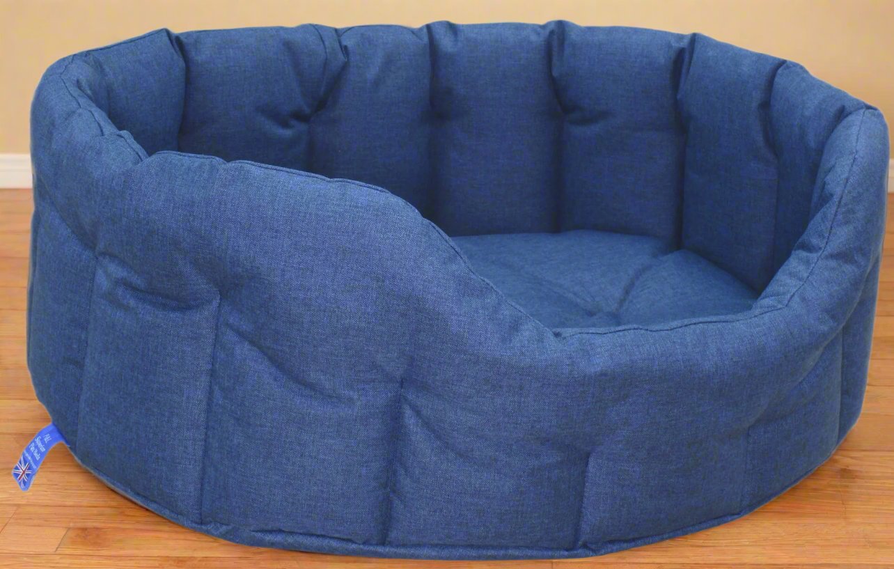 Blue denim waterproof oval dog bed with high padded sides and quilted interior on wooden floor
