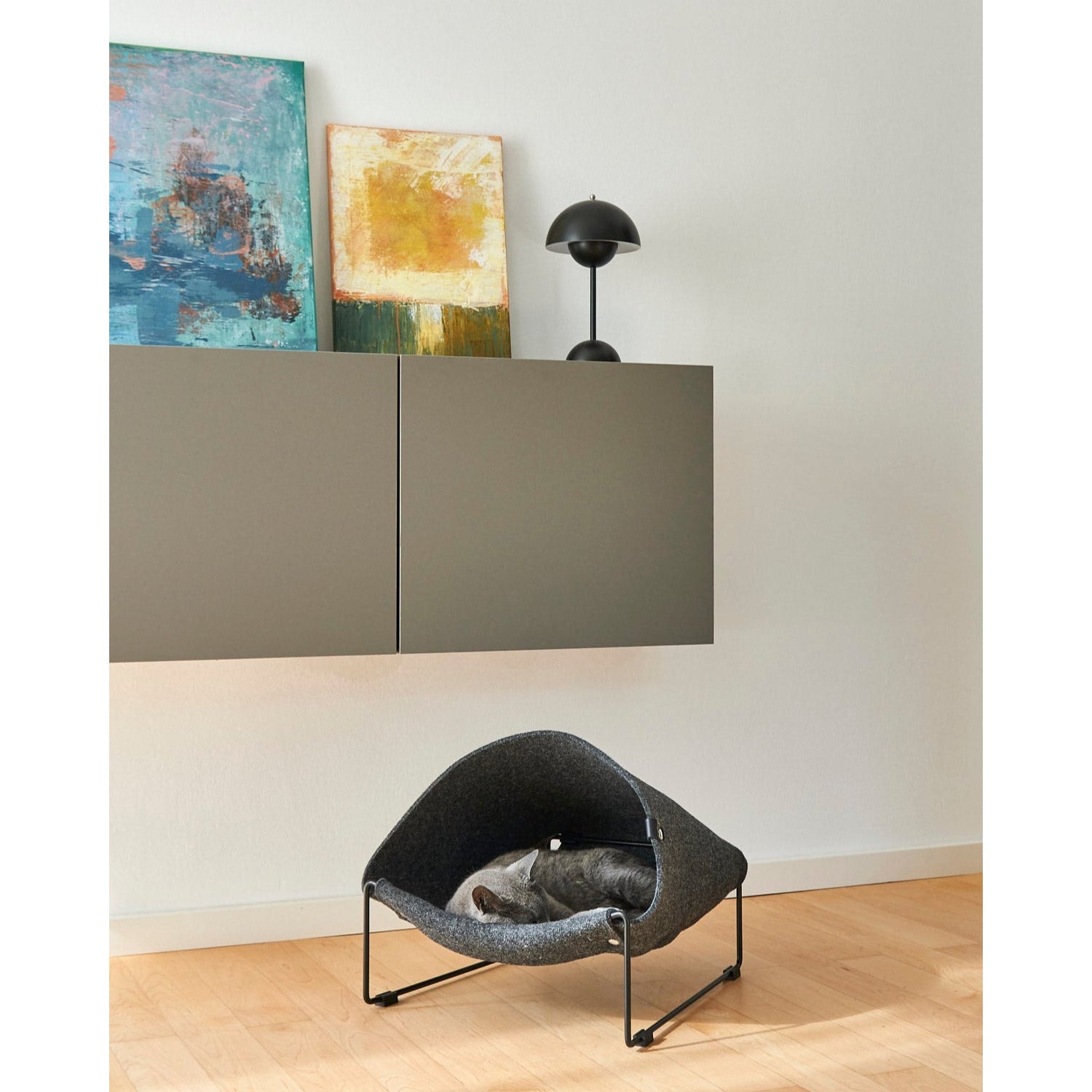 Modern grey Loggia designer cat cave with sleeping cat on wooden floor beside minimalist floating cabinets and artwork