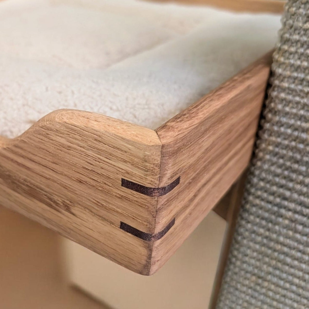 Close-up of the corner of an oak bed frame with a cream cushion beside the sisal carpet post