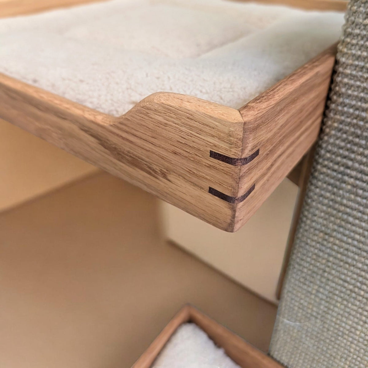 Close-up of the corner of an oak bed frame with a cream cushion beside the sisal carpet post